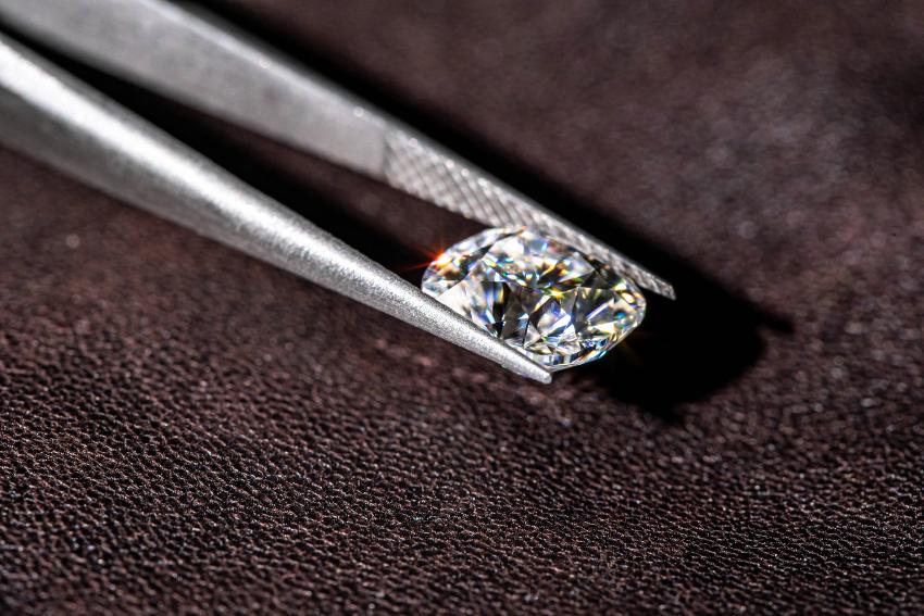 Ein Diamant mit leichtem gelblichen Glanz, der von einer Pinzette gehalten wird 4Cs der Diamanten