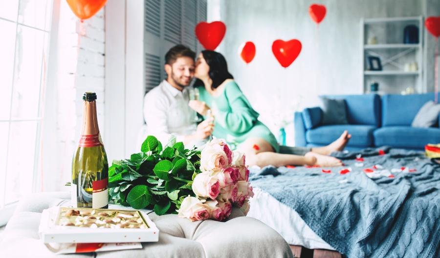 Paar feiert romantisch zuhause im Bett mit Rosen und Sekt