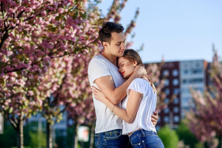 Junges Paar in T-Shirts umarmt sich unter einem blühendem Baum - Heiratsantrag zu Ostern