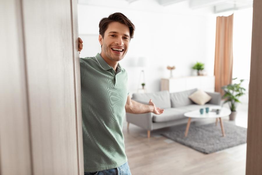 Junger Mann öffnet erfreut die Tür seiner Wohnung