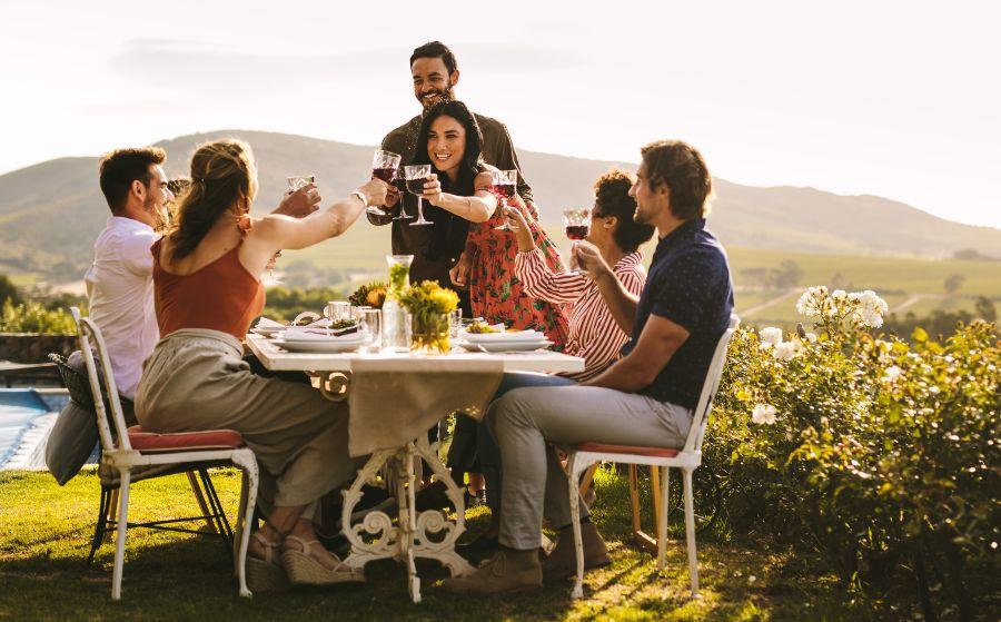 Junge Leute sitzen draußen im Garten, feiern, trinken Wein - Verlobung bekannt geben