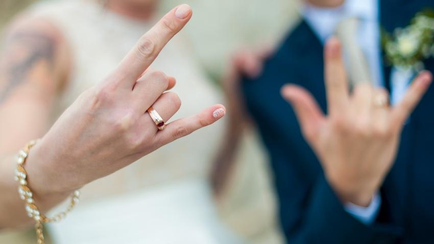 Brautpaar zeigt Eheringe mit Rock ’n’ Roll Zeichen